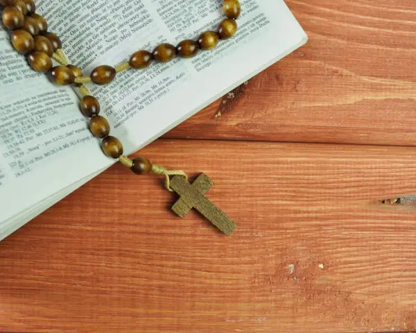 Różaniec na drewnianym stole obok Biblii, przypominający o 10 przykazaniach kościelnych i modlitwie.