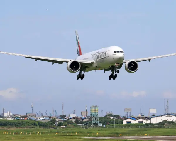 Emirates Boeing 777 zbliża się do lądowania. W tle widać przemysłowy krajobraz i inne samoloty na niebie, sugerujące ruch lotniczy, być może związane z dżerba loty.