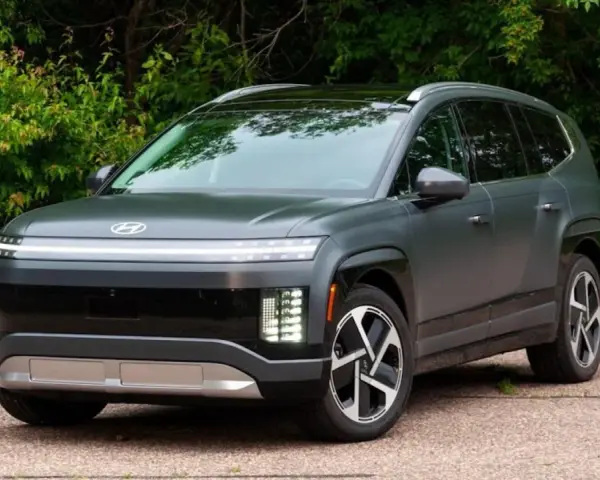 Szary SUV Hyundai IONIQ 9 z charakterystycznym pasem świateł z przodu, na tle zieleni.