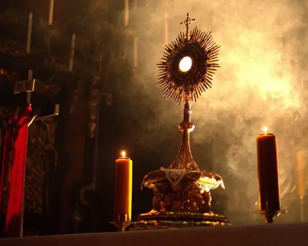 Złota monstrancja z hostią, otoczona płonącymi świecami i dymem, tworzy atmosferę głębokiej adoracji.