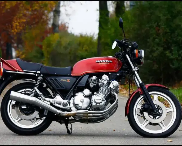 Klasyczny czerwony motocykl Honda CBX 1000 z lat 80. stoi na drodze, otoczony jesienną zielenią i opadłymi liśćmi.