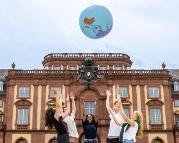 Studierende werfen einen Globus in die Luft vor dem Gebäude des akademischen Auslandsamtes.