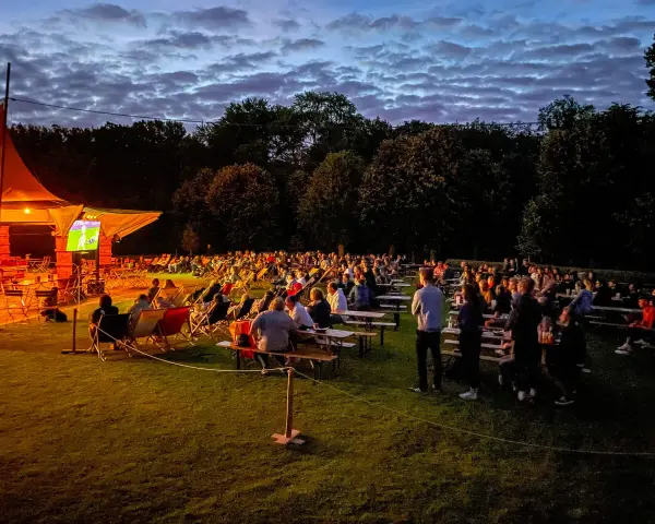 Menschen genießen ein Fußballspiel beim Public Viewing in Berlin unter einem dramatischen Abendhimmel.