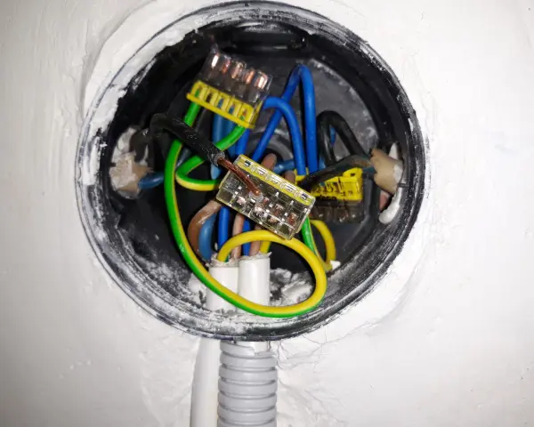 Wnętrze puszki elektrycznej z przewodami: niebieskim, zielono-żółtym i brązowym, połączonymi złączkami. Trwa zerowanie gniazdka.