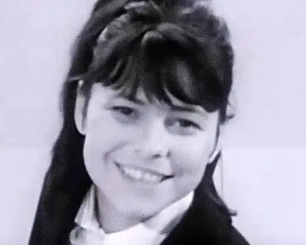 Uśmiechnięta Karin Stanek, jak malowana lala, w czarnym żakiecie i białej koszuli.