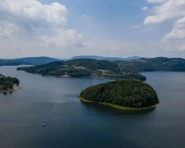 Widok z lotu ptaka na jezioro z wyspą porośniętą lasem i otoczone wzgórzami.
