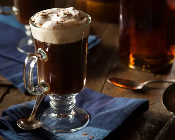 En värmande irish coffee med vispad grädde och kanel på en blå duk.