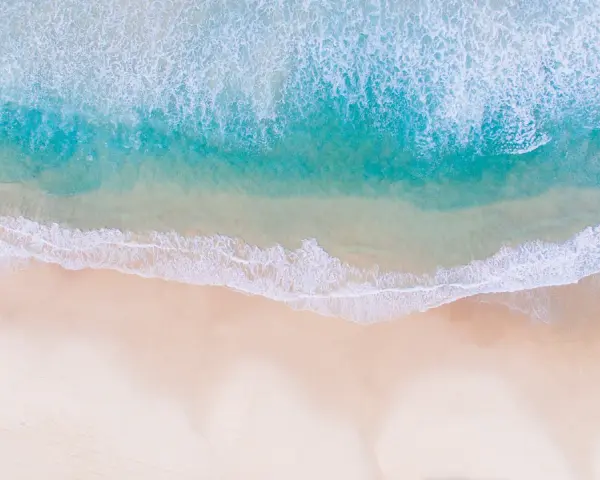 Vue aérienne d'une photo à la plage, avec des vagues turquoise déferlant sur le sable doré.
