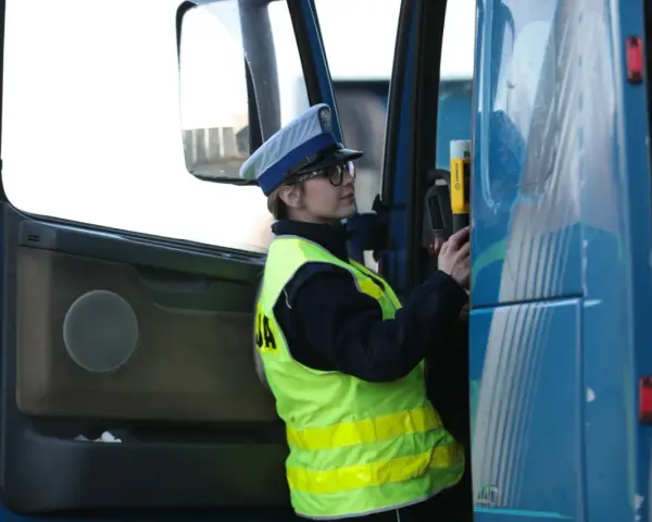 Policjantka w kamizelce odblaskowej i czapce przykłada alkomat do drzwi ciężarówki.