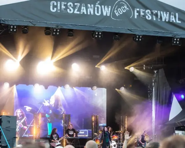 Zespół gra na scenie podczas Cieszanów Rock Festiwal. W tle wielki ekran z wizerunkiem wokalistki i reflektory.