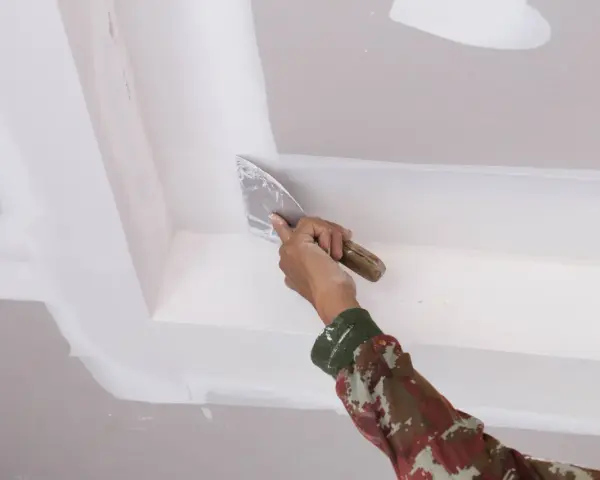 Mano con espátula aplica masilla para pegar escayola rota en el techo.
