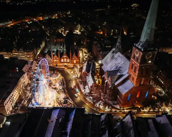 Lichterglanz auf dem Weihnachtsmarkt Schleswig-Holstein: Ein Riesenrad dreht sich neben einer Kirche, während Schneeflocken fallen.
