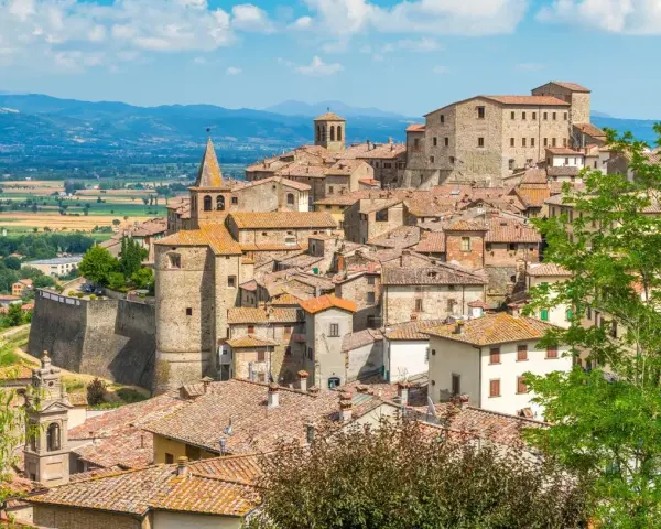 Borgo medievale con tetti in cotto e una torre campanaria, incastonato tra dolci colline verdi. Un luogo che evoca il fascino del **passo dello spino**.