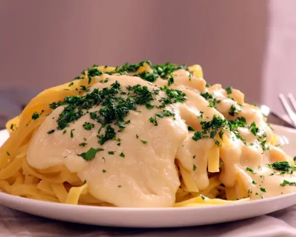 Pasta Alfredo cremosa con perejil picado en un plato blanco.