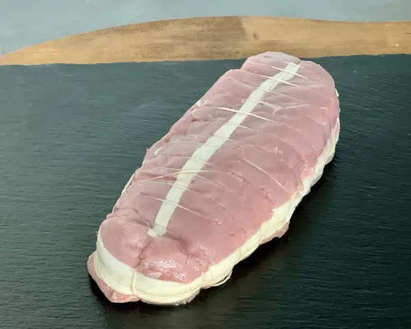 Rôti de veau cru ficelé, prêt à cuire, sur une planche sombre.