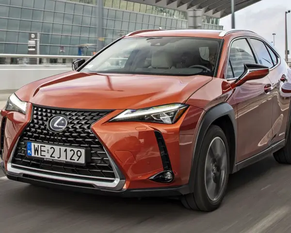 Pomarańczowy Lexus UX 250h w ruchu miejskim, z nowoczesnym grillem i reflektorami LED.