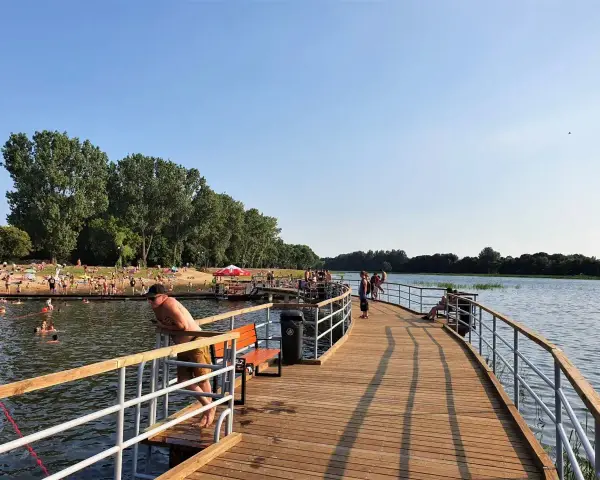 Ludzie odpoczywają i kąpią się nad zalewem Borki. Drewniane molo zaprasza do spacerów i podziwiania widoków.