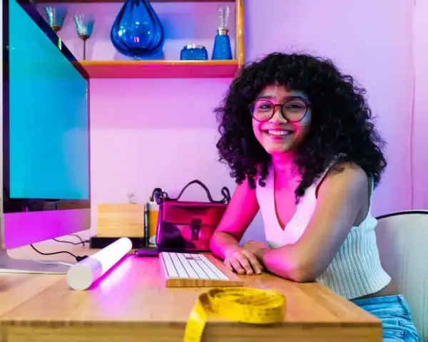 Giovane donna sorridente al computer, pronta a diventare e-commerce manager. Sul tavolo, un metro da sarta giallo.