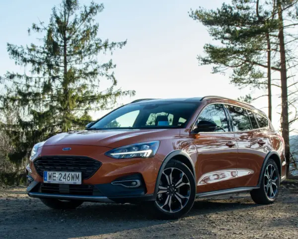Pomarańczowy Ford Focus kombi na tle drzew i nieba.