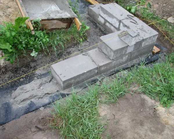 Fundamenty z betonu i bloczków, częściowo zalane, otoczone trawą. Pytanie, czy można zostawić odkryte fundamenty na zimę, jest tu kluczowe.