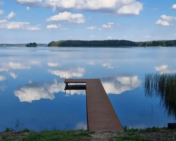 Spokojne jezioro Wągrowiec z drewnianym pomostem odbijającym chmury na błękitnym niebie.