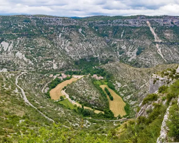 Vue aérienne du cirque de Navacelles, un méandre de rivière creusé dans un paysage de garrigue et de falaises calcaires, avec un village niché au fond.