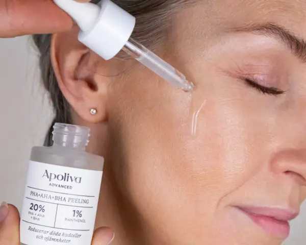 Droppe av aha-syra ansikte-serum appliceras på huden. En flaska med peeling syns i förgrunden.