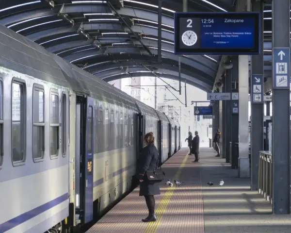 Pociąg na peronie, tablica informacyjna z trasą do Zakopanego, pasażerowie.