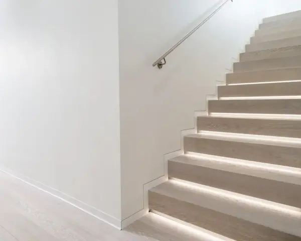 Scala moderna con gradini in legno illuminati e un discreto profilo battiscopa filo muro che ne esalta la pulizia delle linee.