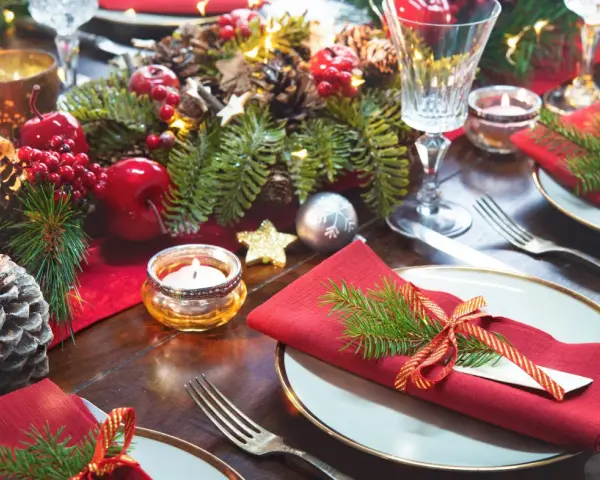 Vackert dukat julbord med röda servetter, granris, äpplen, kottar och ljus. Här ser du vad man har på ett julbord för att skapa julstämning.