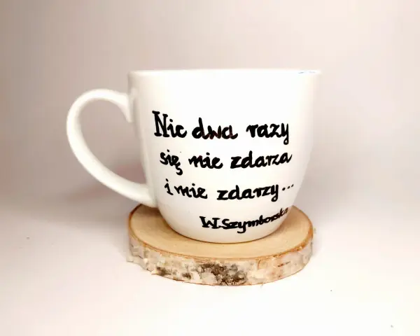 Biały kubek z cytatem Wisławy Szymborskiej: "Nic dwa razy się nie zdarza i nie zdarzy...". Wczoraj kiedy twoje imię ktoś wymówił przy mnie głośno wiersz.