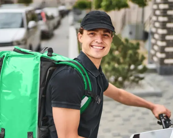 Uśmiechnięty kurier Bolt Food z zieloną torbą na plecach, gotowy do pracy i dobrych zarobków.