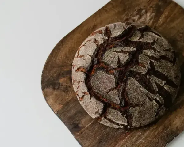 Chleb bez mąki, ciemny, okrągły bochenek z popękaną skórką, leży na drewnianej desce.