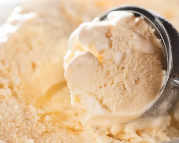 Ein Löffel nimmt eine Kugel cremiges Eis auf. Kleine eiskristalle im eis glitzern im Licht.