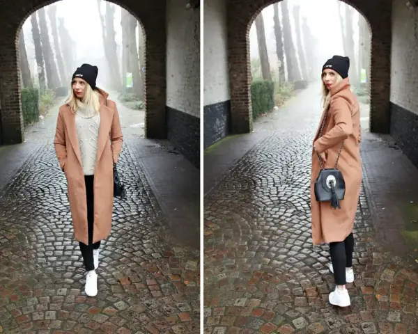Kobieta w płaszczu w kolorze camel i czarnej czapce idzie brukowaną alejką.