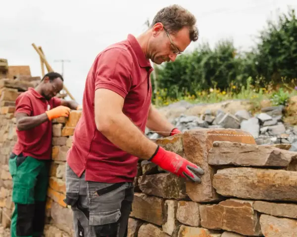 Deux maçons construisent un mur en pierre sèche.