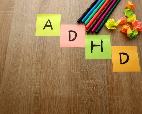 Kolorowe karteczki z literami "A", "D", "H", "D" układają się w napis ADHD. Obok leżą pisaki i pomięte papierki, jakby ktoś próbował znaleźć rozwiązanie, może z pomocą leku Elvanse.