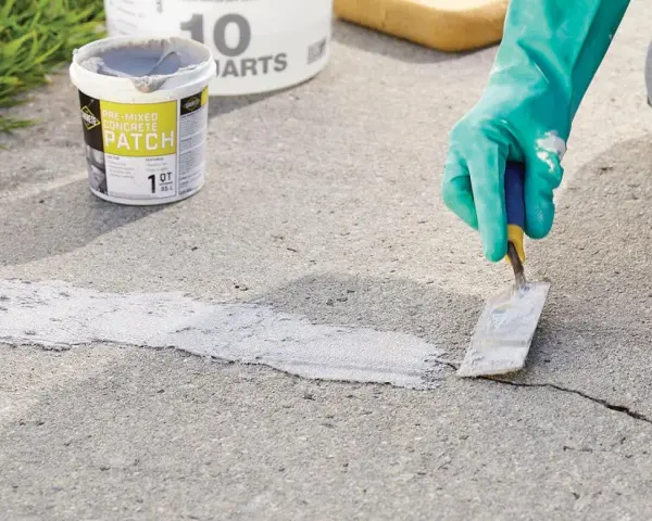 Applying pre-mixed concrete patch to fix cracks in pavement. A gloved hand uses a trowel to smooth the patch.