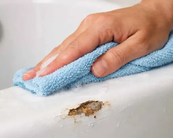 Main d'une personne nettoyant une rayure sur une baignoire en acrylique avec un chiffon bleu.