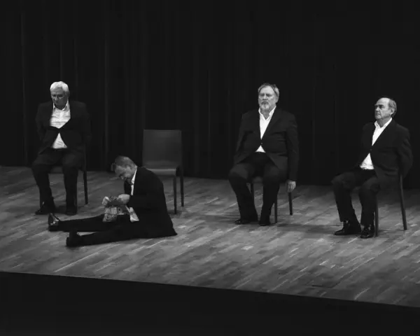 Czterech aktorów w garniturach na scenie. Jeden siedzi na podłodze, pozostali na krzesłach. Kwartet dla czterech aktorów.