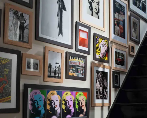 Un mur couvert de tableaux, dont des portraits de Marilyn Monroe, une scène de rue et une affiche de Spider-Man, le tout dans un cadre.
