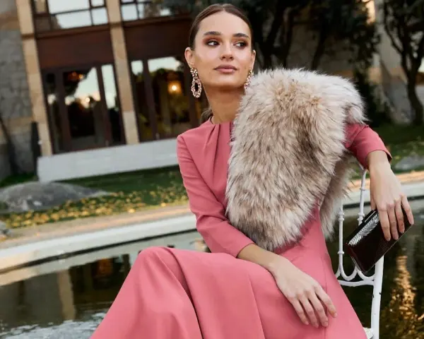Elegante outfit fiesta invierno: vestido rosa palo, chal de pelo y bolso de mano.