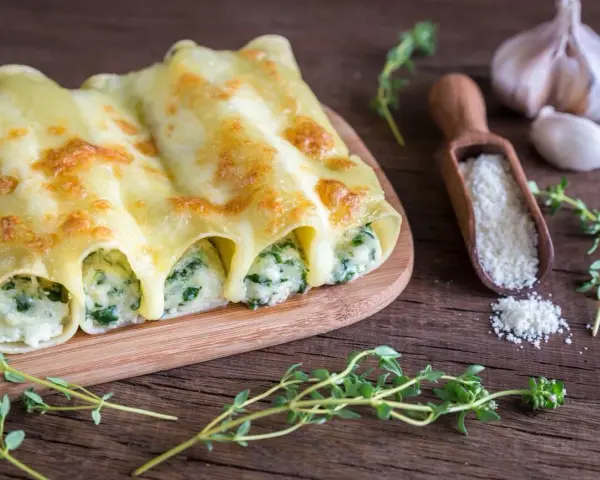 Złociste cannelloni ze szpinakiem, zapieczone pod ciągnącym serem, prezentują się apetycznie na drewnianej desce.