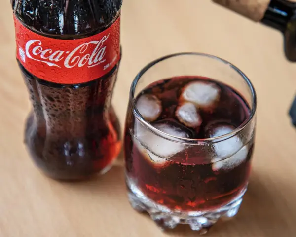 Szklanka z lodem i napojem, obok butelka Coca-Coli. Idealne na gorący dzień, gdy masz ochotę na wino z colą.