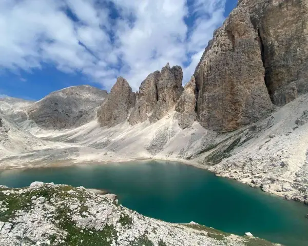 Il **lago di Antermoia**, incastonato tra imponenti vette rocciose, riflette il cielo azzurro e le nuvole bianche. Un gioiello alpino.
