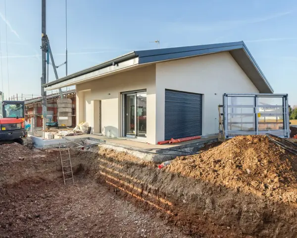 Budowa domu 70m2. Wykop pod fundamenty, koparka i częściowo wykończony budynek.