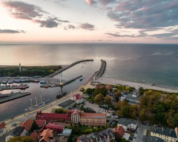 Widok z lotu ptaka na port w Ustce z łodziami i latarnią morską w tle.