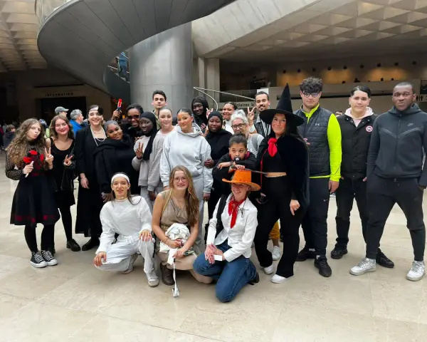 Un groupe de jeunes gens, certains déguisés, pose pour une photo dans un hall moderne.