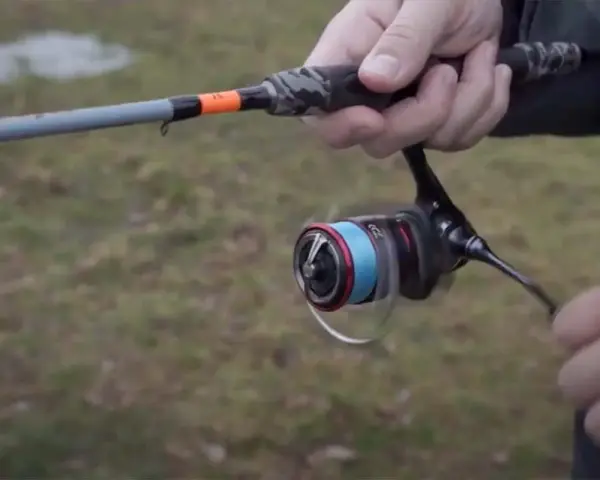 Daiwa Fuego Camo Spin Test: Eine Hand hält eine Angelrute mit Camo-Griff und einer Rolle mit blauer Schnur.