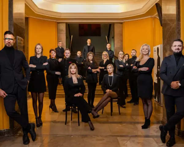 Grupa profesjonalistów w czarnych strojach pozuje w eleganckim wnętrzu.
